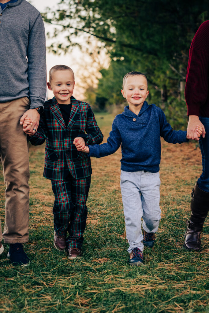 Two young boys holding hands and walking toward camera during outdoor fall mini session in Madison Wisconsin.