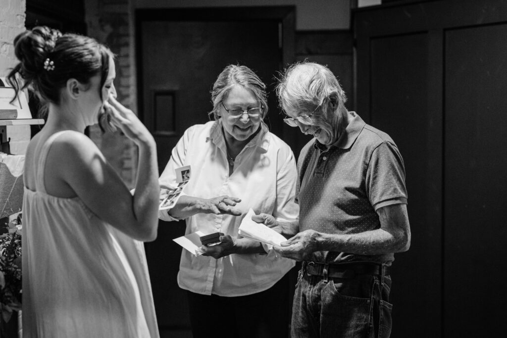 Black and white photo of older family members looking at printed photographs together during wedding preparations.