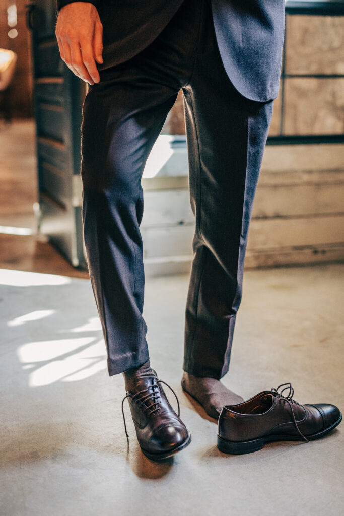 Groom stepping into black leather dress shoes while getting ready inside a historic Wisconsin wedding venue.