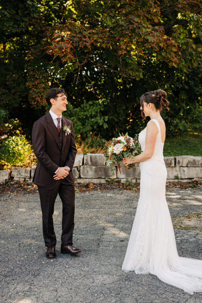 Bride and groom facing each other during an outdoor first look with fall greenery at a Wisconsin wedding.