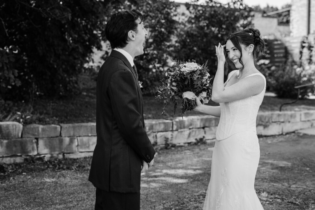 Black and white photo of bride and groom laughing together during their first look outside The Lageret.