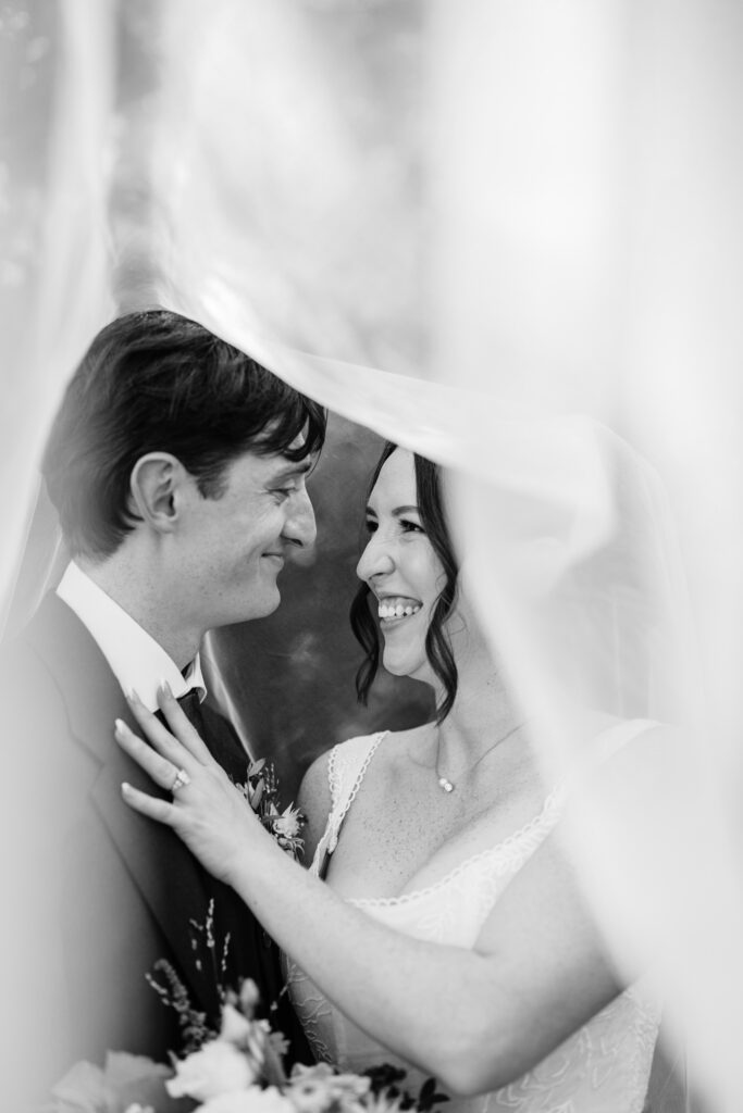 Black and white photo of bride and groom smiling at each other beneath the veil during a Wisconsin wedding.