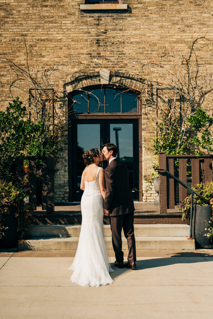 Bride and groom kissing on the steps outside The Lageret wedding venue on a sunny fall day.
