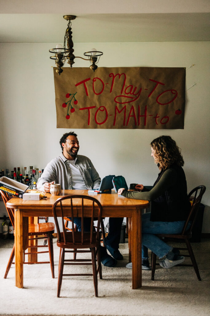 Two people seated across from each other at a dining table, playing a board game in a cozy home setting.