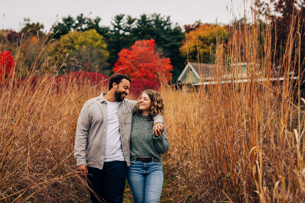 Engaged couple walking together along a grassy path at Aldo Leopold Nature Center, arms around each other.