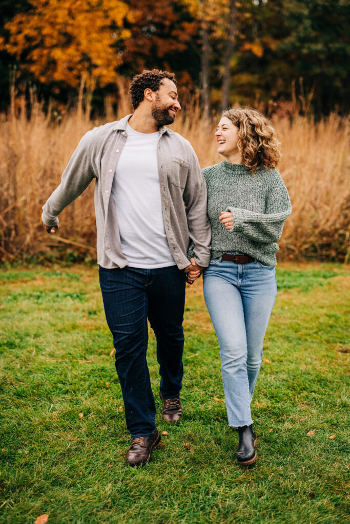 Engaged couple walking hand in hand through an open field at Aldo Leopold Nature Center during autumn.