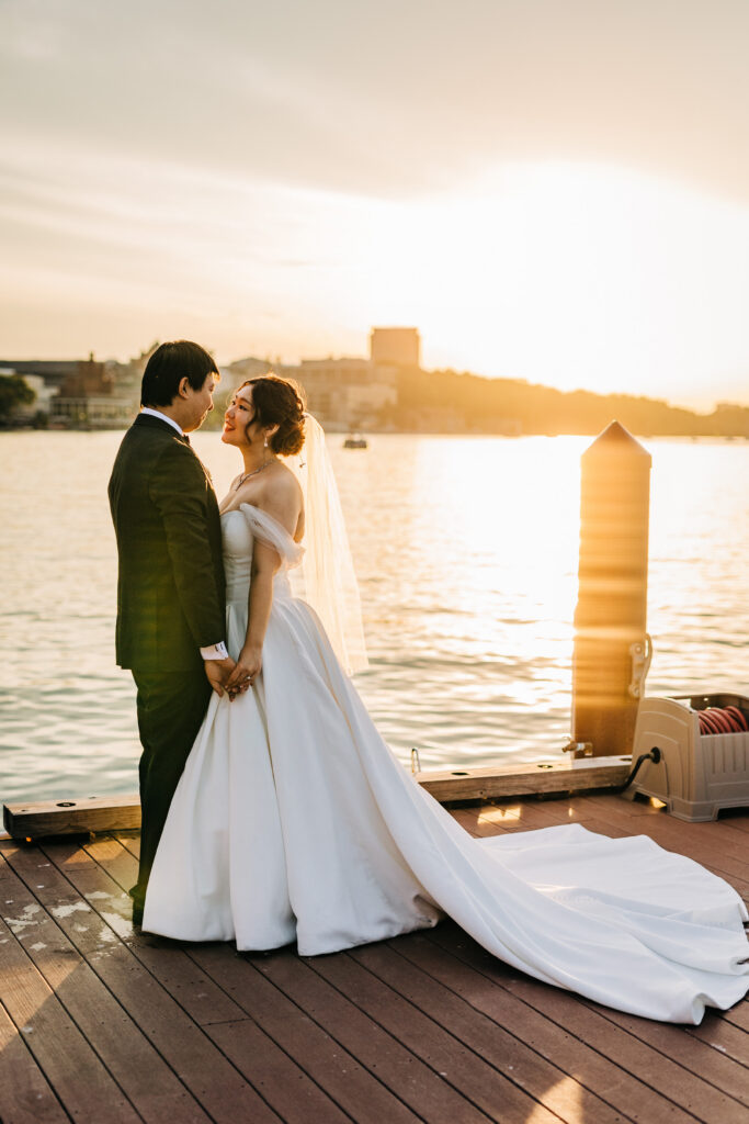 Bride and groom standing on dock at sunset during Edgewater wedding in Madison with warm light over Lake Mendota.