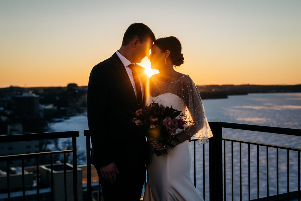 Bride and groom standing close on balcony at sunset overlooking Lake Mendota during Edgewater wedding in Madison.