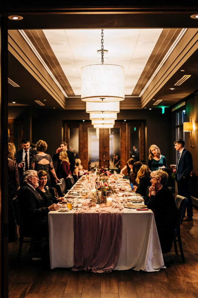Guests seated at long candlelit table during intimate wedding reception at Edgewater in Madison with modern lighting overhead.