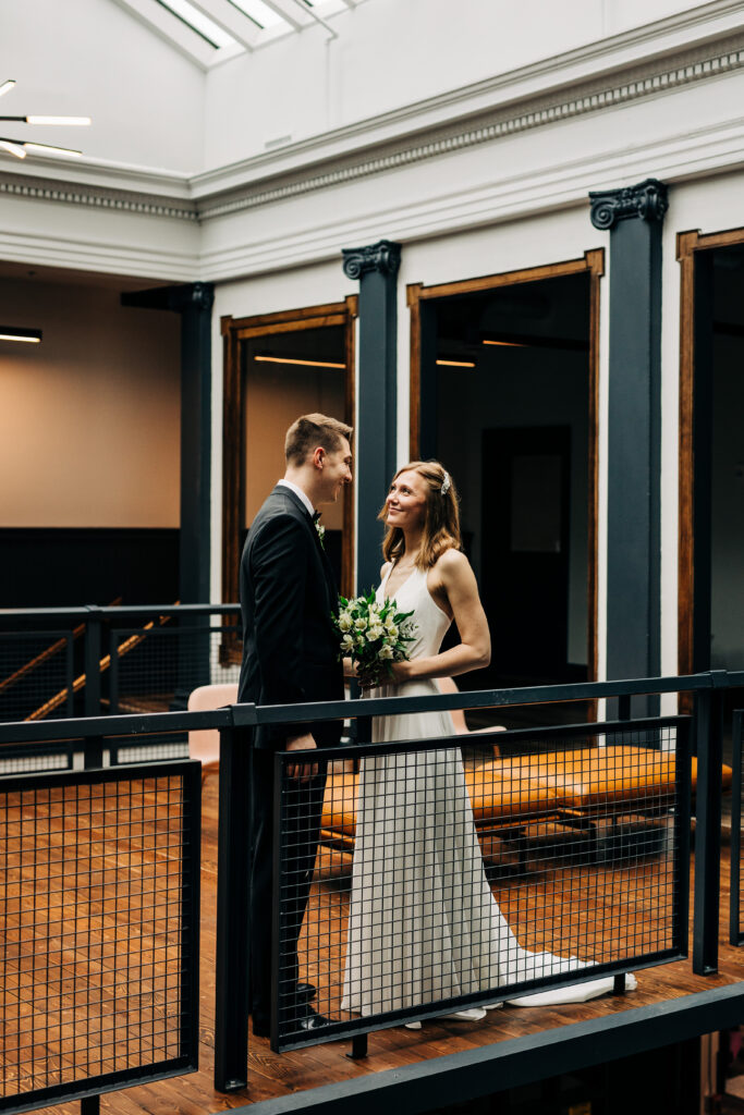 Bride and groom facing each other on indoor balcony at Ellsworth Block wedding venue in Madison with modern industrial details.