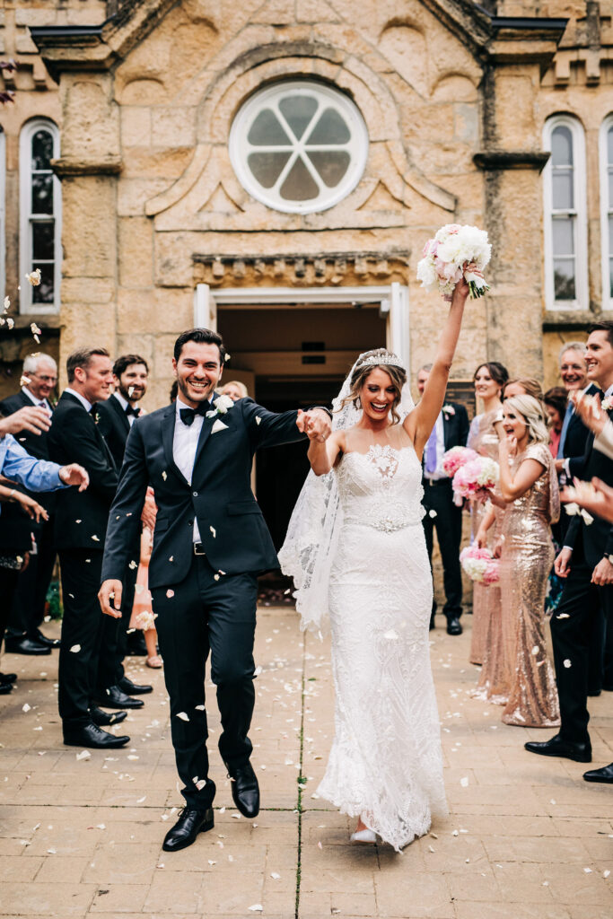 Bride and groom walking through cheering guests during confetti exit outside Gates of Heaven wedding in Madison.