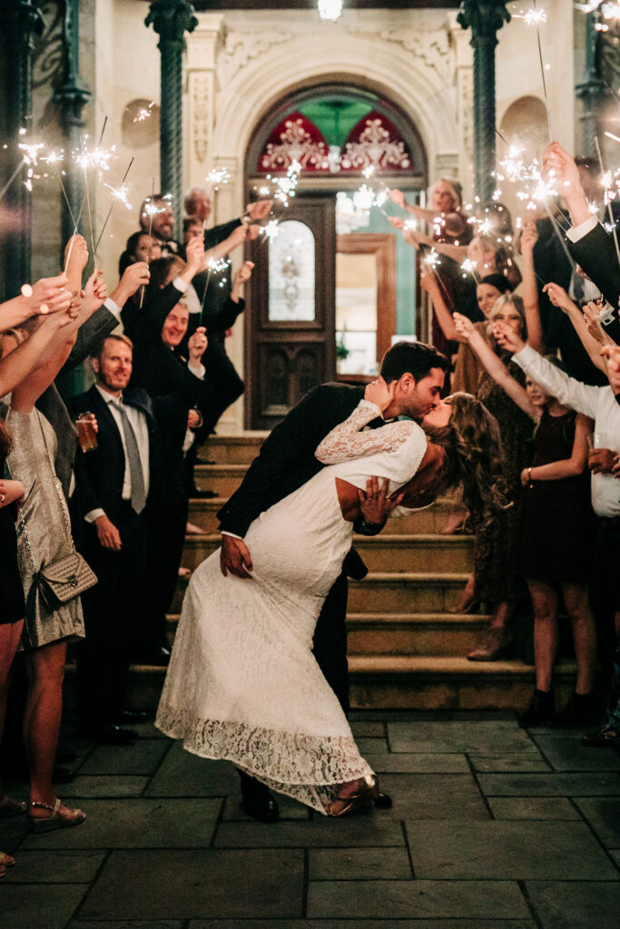 Bride and groom kissing during sparkler exit outside Mansion Hill Inn wedding in Madison as guests hold sparklers.