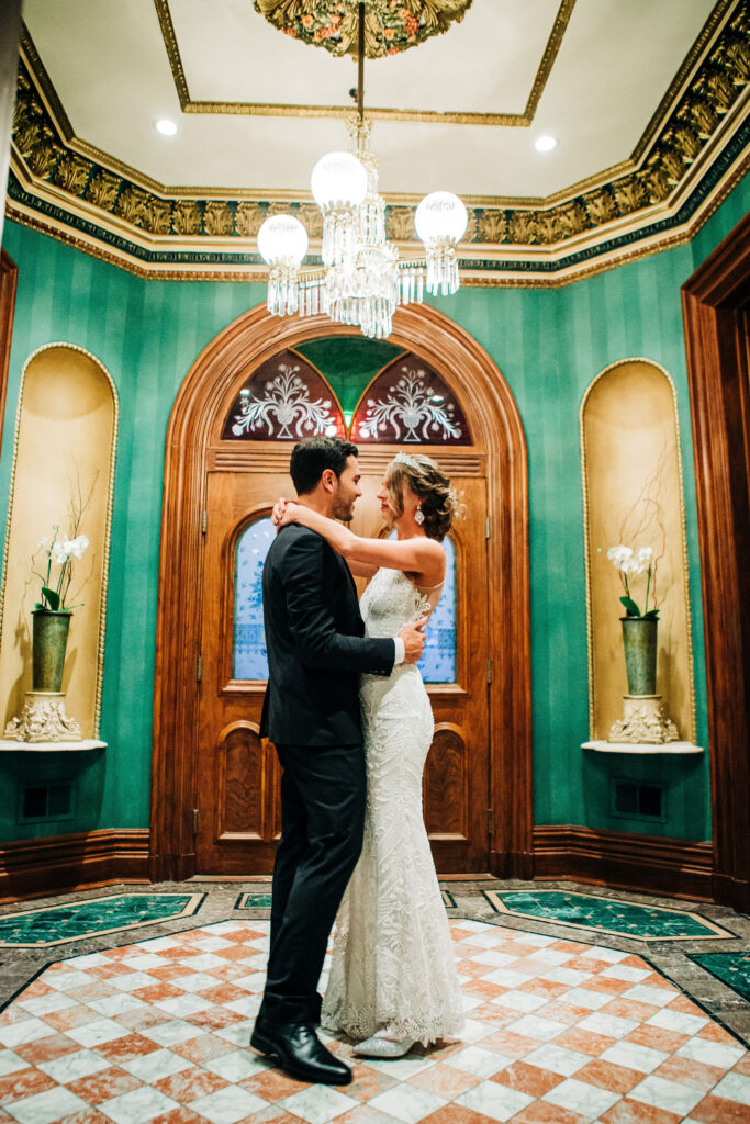 Bride and groom embracing in ornate room with chandelier at Mansion Hill Inn wedding venue in Madison.