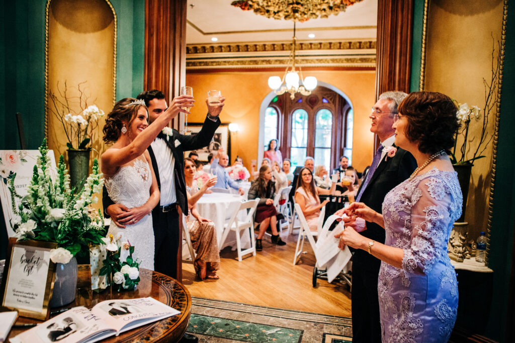 Bride and groom raising glasses during intimate reception toast at Mansion Hill Inn wedding in Madison with guests seated.
