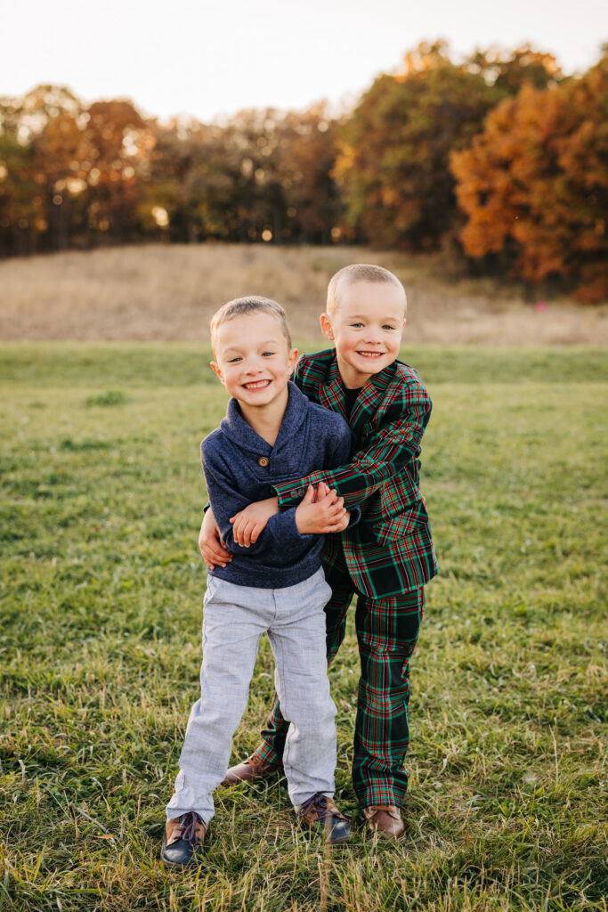 Two young boys smiling and hugging in a grassy field during fall family mini session in Madison, Wisconsin