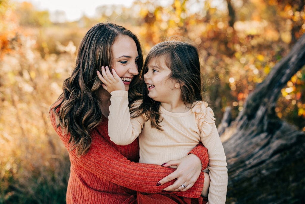 Mother holding young daughter close as they smile at each other during golden hour fall session in Madison WI.