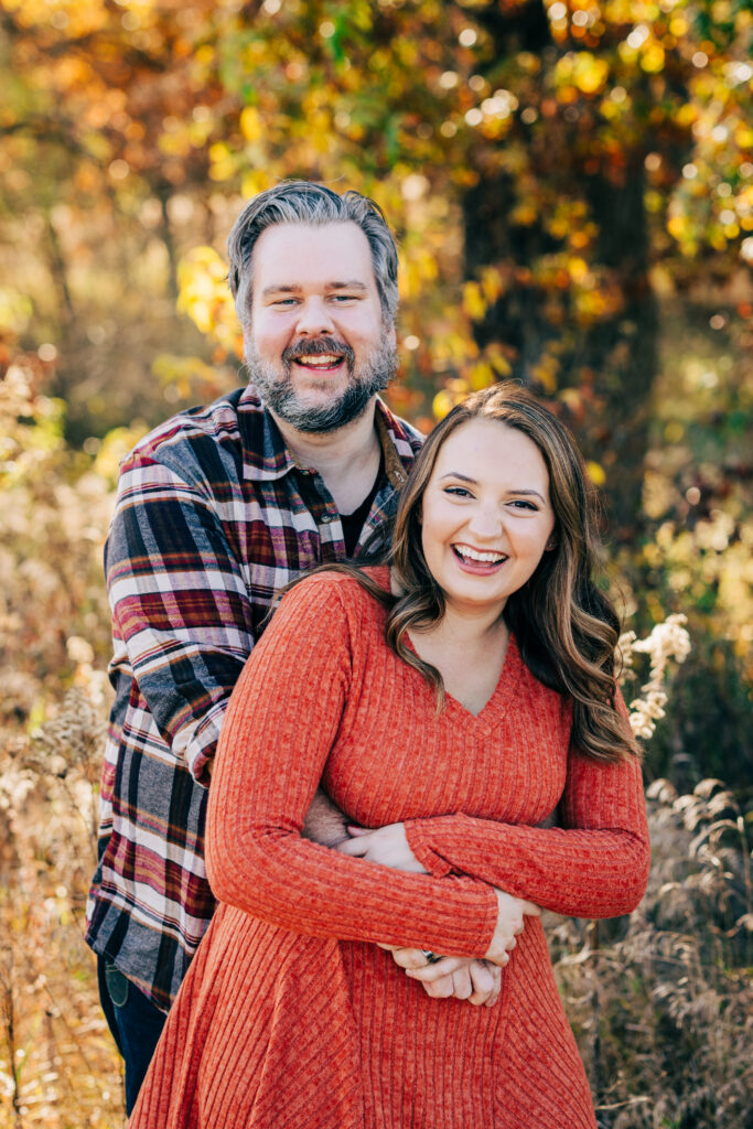 Couple embracing and smiling outdoors with warm fall colors during Madison Wisconsin family mini session.
