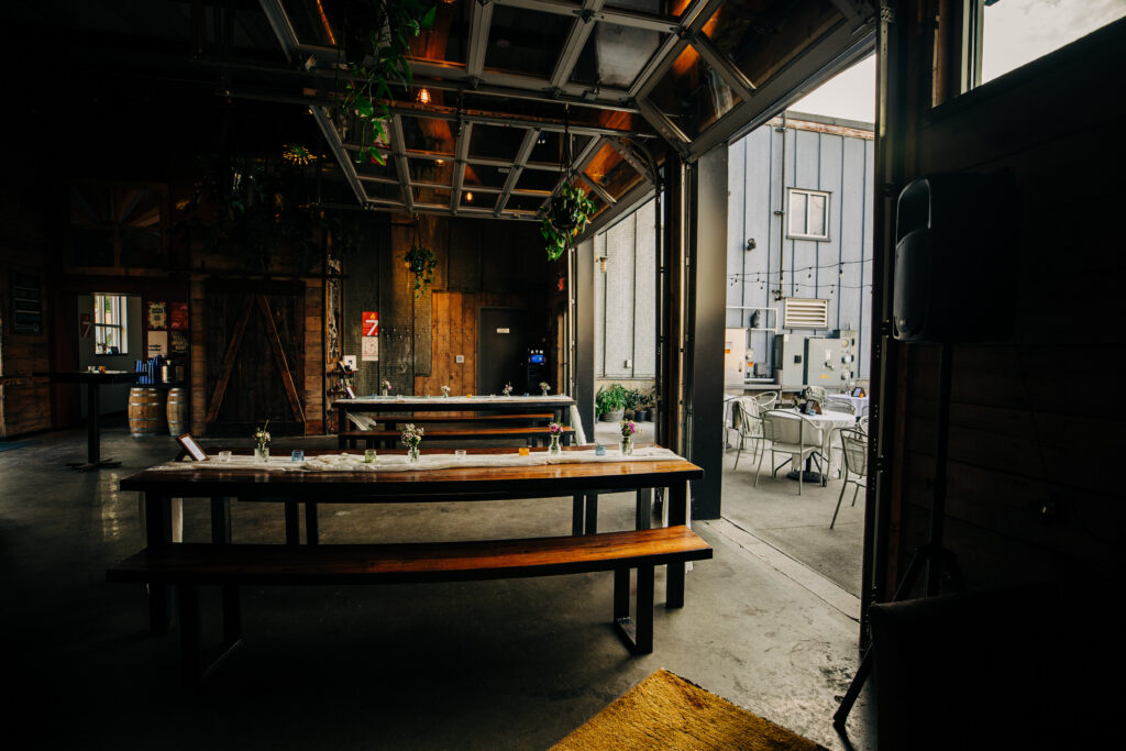 Industrial wedding reception space at State Line Distillery in Madison with long wooden tables and open garage door.