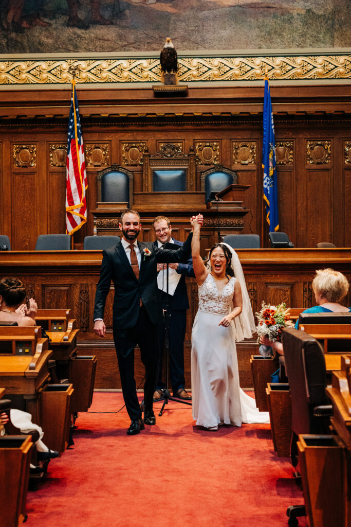 Bride and groom walking up aisle with raised hands after ceremony at Wisconsin State Capitol intimate wedding in Madison.