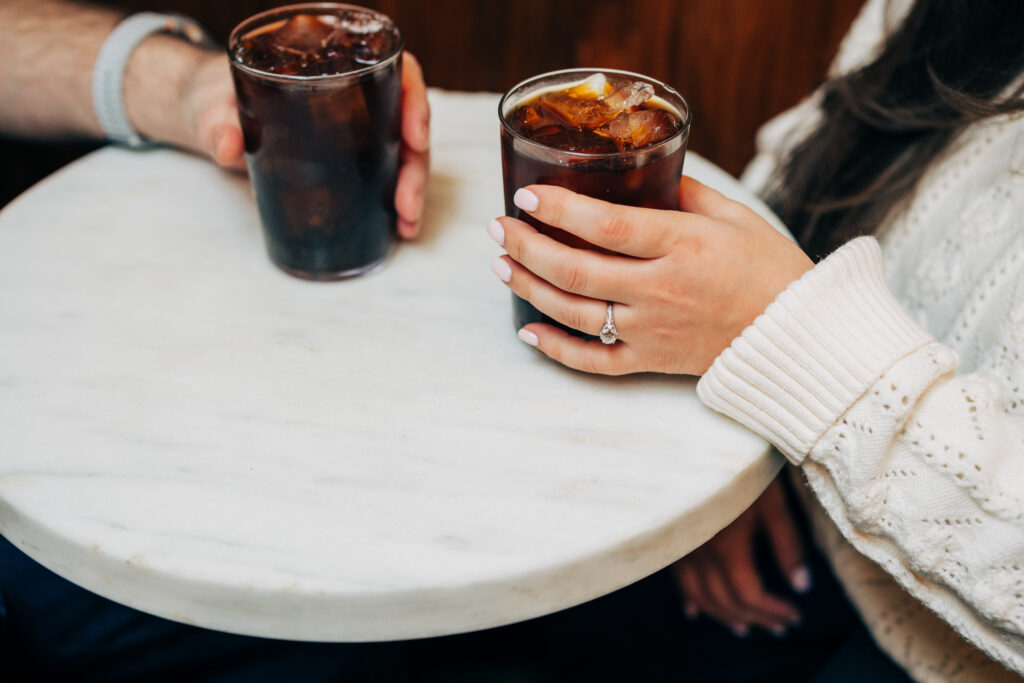 Couple holding iced coffee drinks during an engagement session at Leopold's Books Bar Caffè in Madison, WI.