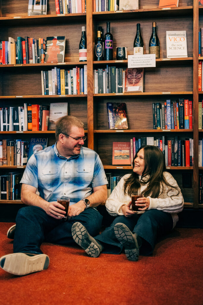 Couple sitting in front of bookshelves with coffee during their engagement photos in Madison, WI.
