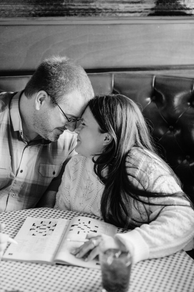 Couple with heads together lovingly doing a crossword puzzle at table with iced tea at Leopold’s Book Bar and Caffe in Madison, WI.