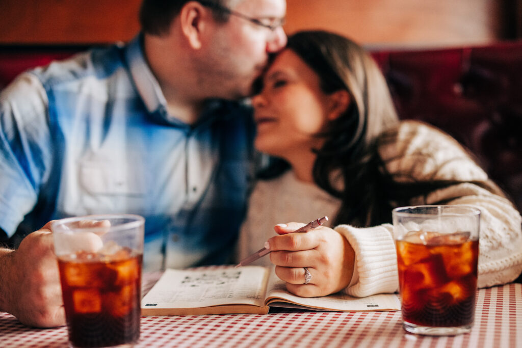Man kissing woman's forehead while sitting at a table doing a crossword puzzle at Leopold's Books Bar Caffè in Madison, WI.