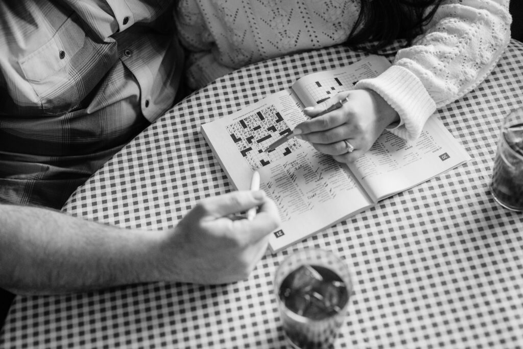 Couple doing a crossword puzzle together at table during their engagement session at Leopold's Books Bar Caffè in Madison, WI.