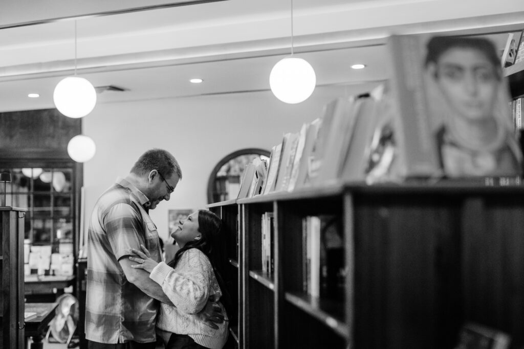 Couple embraced by bookshelves at Leopold's Books Bar Caffè during Leopolds Madison engagement session in Madison, WI