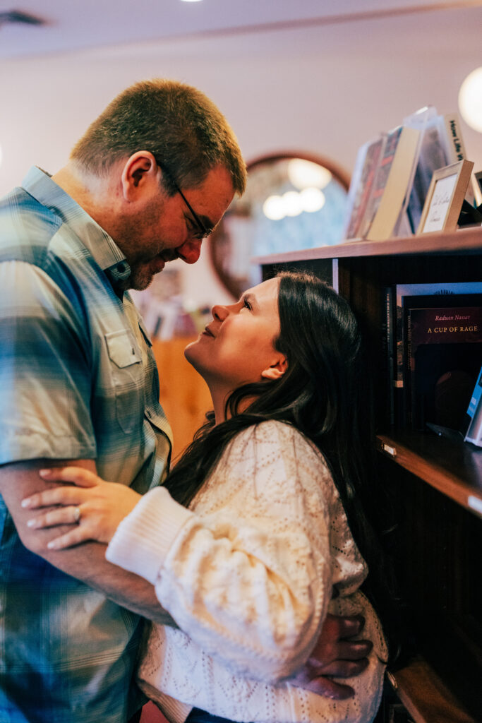 Couple facing each other and smiling by books at Leopold's Books Bar Caffè during Leopolds Madison engagement session in Madison, WI