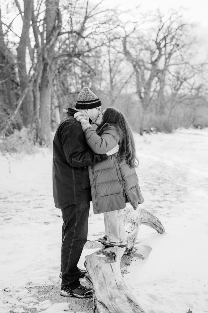 Couple kissing by log and trees in the snow during engagement session at Picnic Point