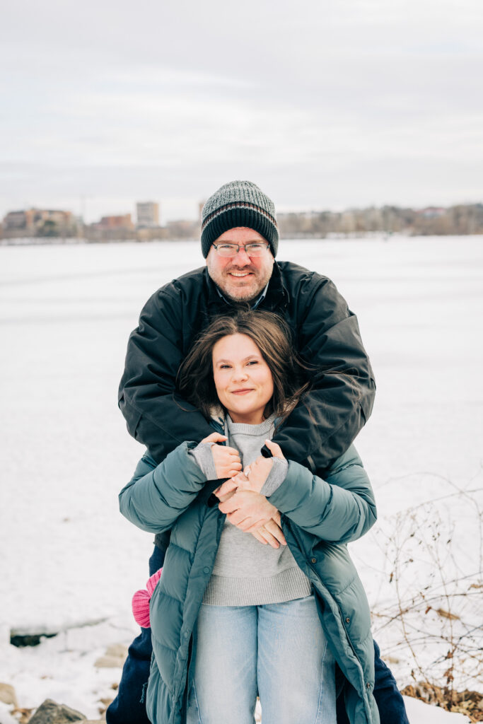 Couple standing in front of frozen lake during engagement session at Picnic Point