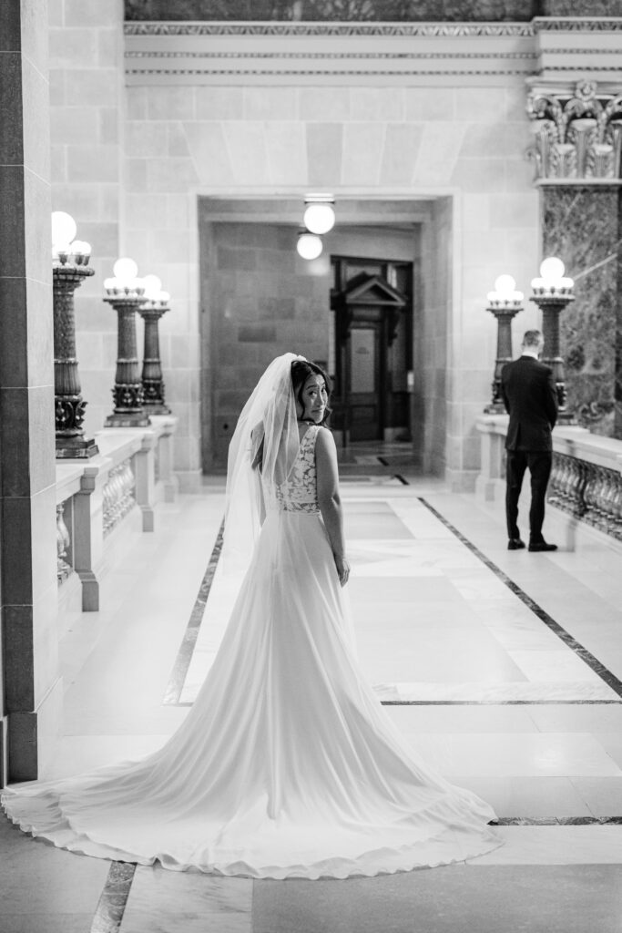 Bride in flowing wedding gown looking back in the Wisconsin State Capitol hallway during Madison wedding portraits.
