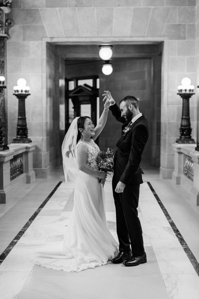 Groom twirling bride during playful wedding portraits beneath glowing lights at the Wisconsin State Capitol.