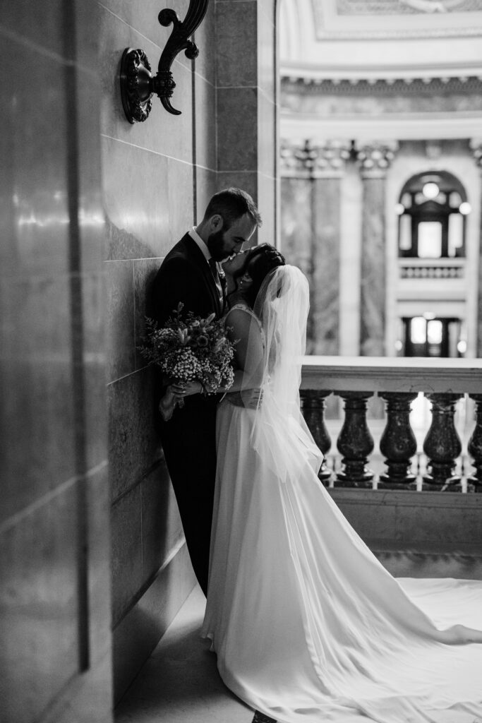 Bride and groom kissing beside marble walls during intimate Capitol wedding portraits in Madison, Wisconsin.