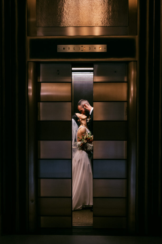 Bride and groom kissing inside a vintage elevator during creative Wisconsin Capitol wedding portraits.