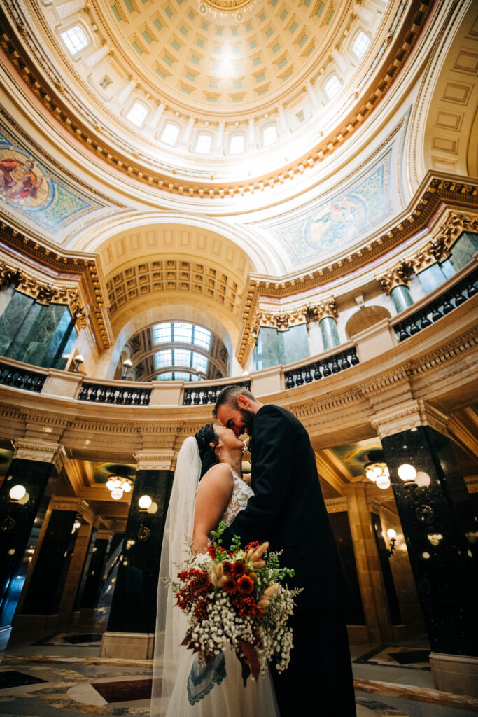 Newlyweds embracing beneath the domed rotunda inside the Wisconsin State Capitol building in Madison.