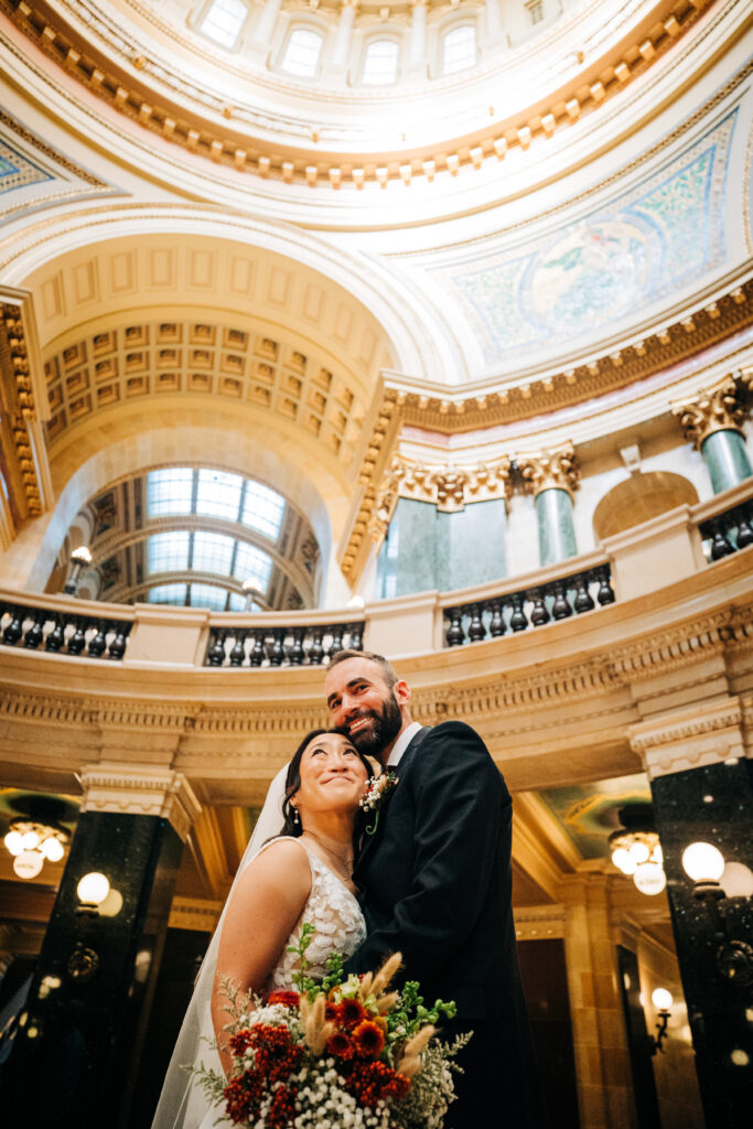 Bride and groom smiling together under the ornate Capitol dome during Madison wedding portraits.