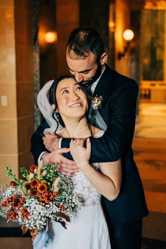 Bride and groom embracing indoors at the Wisconsin State Capitol with warm golden lighting and autumn wedding bouquet.