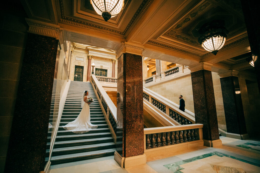 Bride and groom posed on grand marble staircases inside the Wisconsin State Capitol wedding venue.