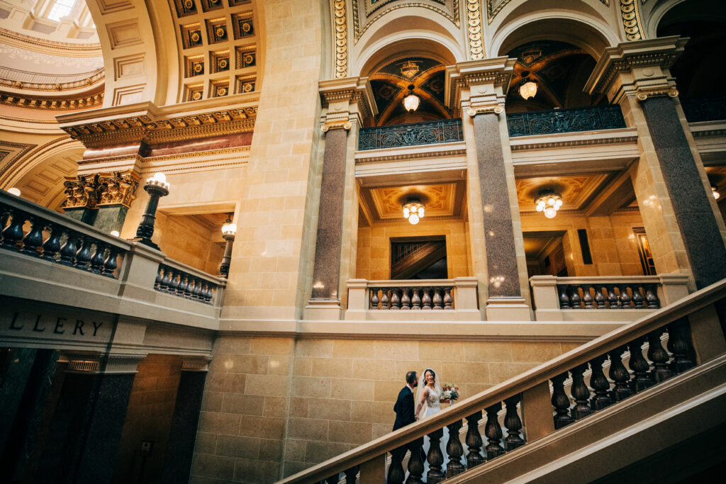 Couple walking along ornate Capitol staircase during elegant Wisconsin Capitol wedding portraits.