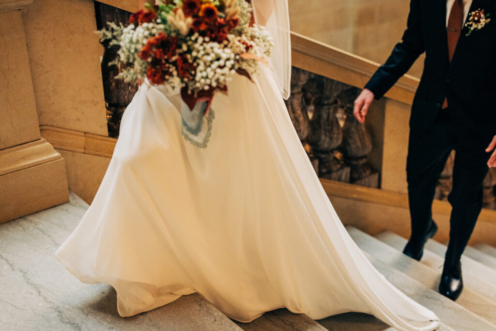 Flowing bridal gown and bouquet captured on marble stairs inside the Wisconsin State Capitol.
