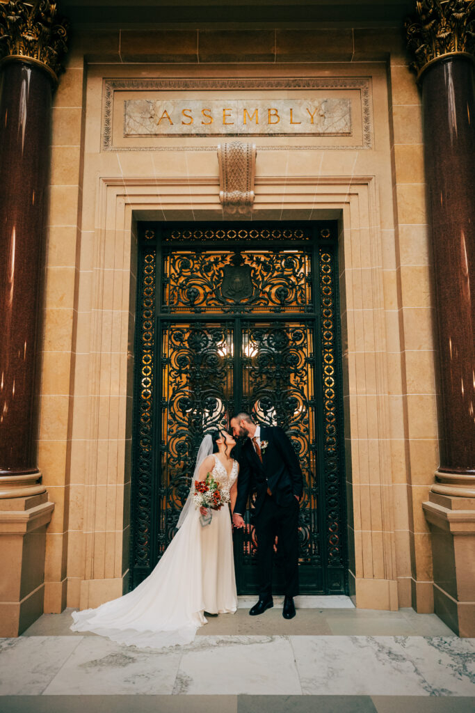Bride and groom holding hands in front of ornate Assembly chamber doors at Wisconsin State Capitol.