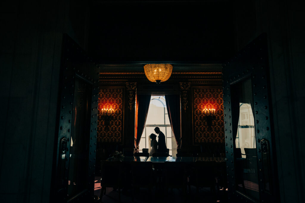 Silhouette portrait of bride and groom framed by tall windows inside elegant Capitol meeting room.