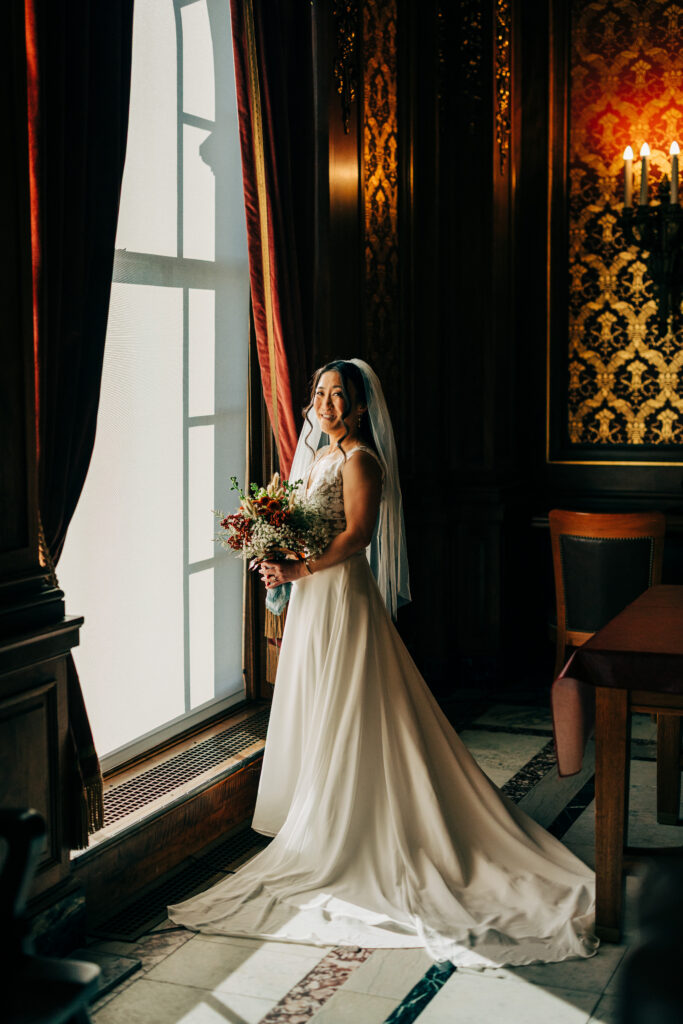 Bride standing beside tall window with bouquet inside the Wisconsin State Capitol wedding venue.