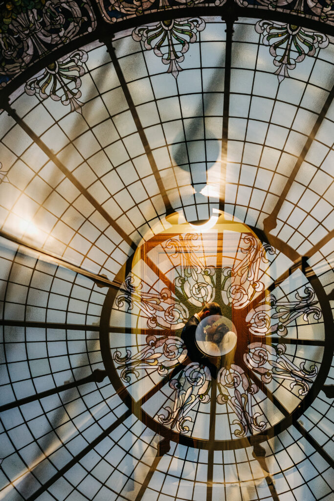 Creative reflection portrait of bride and groom beneath stained-glass dome inside Wisconsin State Capitol.