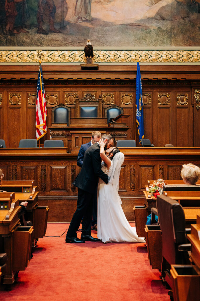 Bride and groom sharing their first kiss during a courthouse wedding ceremony inside a historic courtroom.