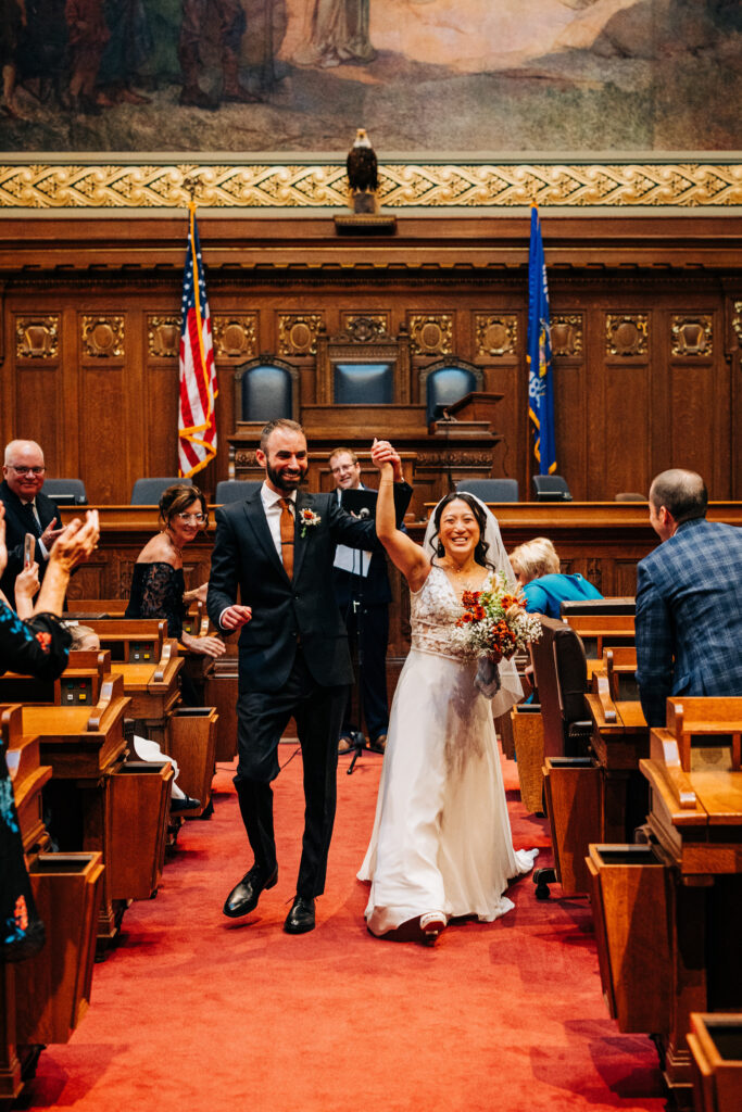 Newly married couple walking down the aisle together after their courthouse wedding ceremony as guests applaud.