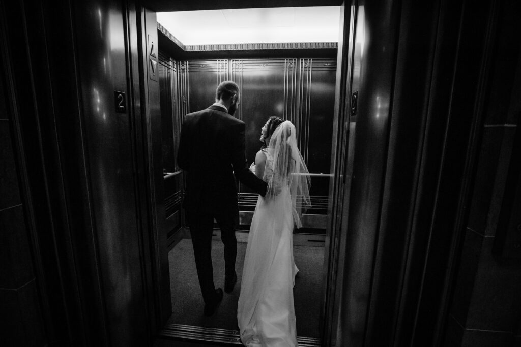 Bride and groom entering a vintage elevator together after their courthouse wedding ceremony in black and white.