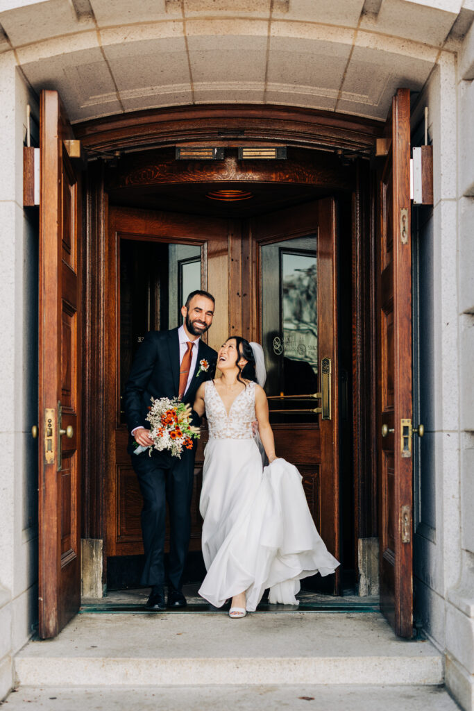 Newly married couple walking out of historic courthouse doors together holding a bouquet after their ceremony.